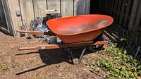 Full side view of the Meaford wheelbarrow showing red metal basket, wooden handles, and metal frame.