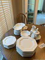 Overview of entire set on table: stacks of hexagonal plates, bowls, teapot, creamer and sugar bowl