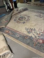 Oval wool rug partly rolled showing floral border design with pink, green, ivory colors on wool pile