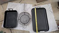 Photo showing All-Clad cast iron skillet, round grilling basket, and rectangular baking pan laid on a cloth