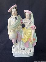 Front view of antique English porcelain figurine depicting a man and woman in pastel-colored period clothing.
