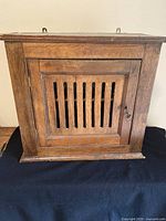 Front view of antique oak hanging cupboard with closed slatted door and metal keyhole.