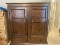 Front view of large antique oak cupboard with two double paneled doors closed, showing wood grain and panel details.