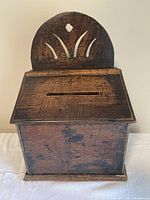Front view of antique oak hanging box with hinged lid and slot, showing decorative cutout back panel.