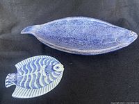 Top view of large deep blue ceramic fish-shaped platter and smaller blue and white fish-shaped trivet on black background.