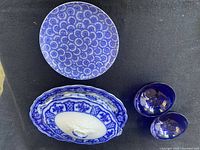 Top view of blue patterned round plate, oval serving platter, and two small blue bowls on black background