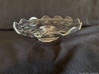 Side angle showing the scalloped edge and low pedestal base of clear glass cake stand.