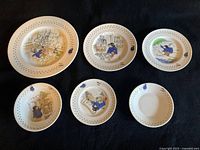 Six plates arranged on black surface showing various Paddington Bear scenes and paw print borders.