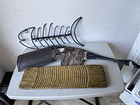 Photo showing metal fish clothes rack, pine wood washboard, antique metal grater, and wooden goose hanging on gray plastic table.