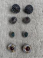 Top view of four pairs of clip-on earrings arranged in two rows on light carpet, showing design details
