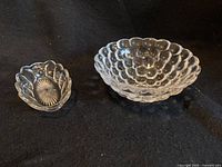 Two clear glass serving bowls with bubble-like patterns, one larger and one smaller, on a dark surface.