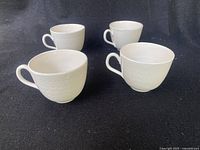 Four large white ceramic teacups with embossed pattern shown on black background.