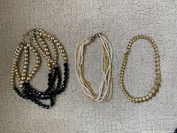 Three necklaces laid flat on a neutral background showing different styles of gold-tone beads and black and white bead accents.