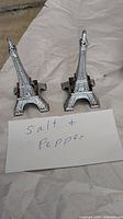 Two metal Eiffel Tower-shaped salt and pepper shakers photographed with a handwritten label.