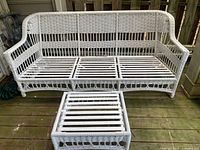 White wicker patio couch frame and matching ottoman without cushions, showing the base slats.