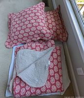 Reversible queen bedspread folded with two large matching pillows on top, showing floral red and cream pattern on one side and neutral quilted reverse.