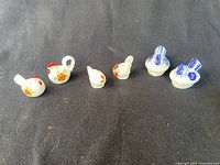 Overview of all three pairs of rooster and hen salt and pepper shakers lined up on black background.
