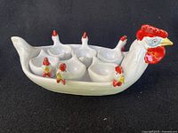 Front view of ceramic hen-shaped serving tray holding six rooster-shaped egg cups.