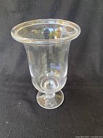 Clear glass vase with wide rim and pedestal base against black background, showing overall shape and size.