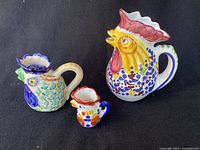 Photo showing all three colorful ceramic rooster jugs together on a black background.