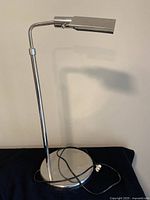 Full view of the lamp showing its adjustable arm, circular base, and rectangular shade in polished metal finish.