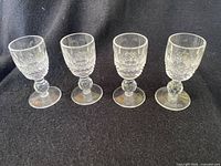 Four vintage Waterford Lismore cordial glasses displayed upright on a black cloth background showing their detailed cut crystal pattern and short stems with round feet.