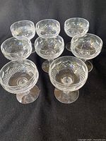 Top angled view showing all 8 clear Waterford Lismore crystal compotes placed together on a black surface, highlighting the diamond and wedge cut pattern on the bowls and the stems.