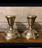 Front view of two sterling silver weighted candlesticks on wood surface with a weathered wooden background.