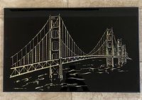Full view of the framed wall art showing the Golden Gate Bridge illustration in gold on a black background.
