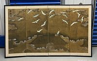 Full view of the four-panel folding screen depicting flying cranes, clouds, and traditional rooftops on a gold background.