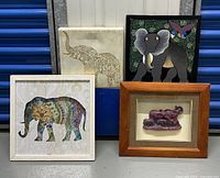 Photo showing four framed elephant-themed wall art pieces in various styles and materials on a blue storage container background.