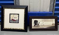 Two framed wall art pieces shown against a blue and metal background, one square with bathtub illustration and one rectangular with chair and text design