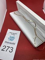 Flat gold chain displayed inside white jewelry box against red background