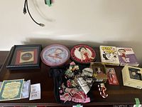 Full overview of all 11 Betty Boop memorabilia pieces laid out on table, including clocks, framed pin, t-shirt, playing cards, figurines, and collectible boxes.