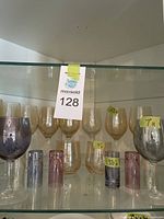 Glassware set displayed on a shelf shows multiple glasses including yellow crackle wine glasses and smaller colored shot glasses.