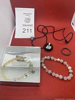 Photo showing the necklace with black cord and pendant, rose quartz bracelet with pearls, and one black ring.