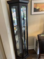 Full view of wooden curio cabinet showing dark wood frame, glass door, and four glass shelves inside, placed in a living or dining room corner.