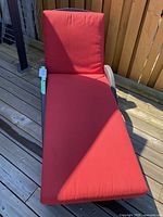 Full view of the deck lounger with a red cushion placed on a wooden deck.