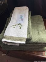 Stack of three green bath towels with a white hand towel embroidered with green leaves and green border on top.