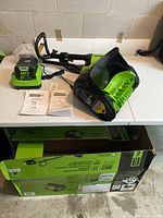 Overview of snow shovel, battery, charger, and manuals on table