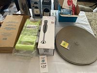 Overview of the lot showing the boxed hand blender, mandolin slicer, boxed mini maker grill, 8 placemats, and Graty salt and pepper grinders.