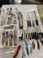 Wide view of entire cutlery set and kitchen utensils on table including various knives, forks, spoons, peelers, and other tools.