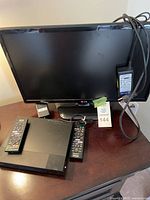 LG 21-inch TV with Sony Blu-ray player and two remote controls on dark brown wooden table. Power cable draped over the TV screen.