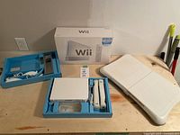 Overview of the Nintendo Wii console, original box, balance board, and controller accessories arranged on a table.