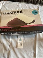 Box of NukNuuk ladies' leather slippers size 10 with sheepskin lining shown on plain cloth background, unopened.