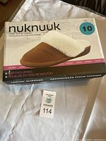 Box of Nuknuuk ladies' leather slippers showing brand, size 10, sheepskin lining, with product image on box top.