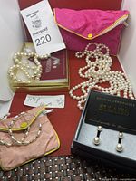 Overview of the lot showing three pearl necklaces, two pink pouches, two pairs of earrings and a certificate in Sllaiss box