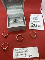 Five rings displayed on red background with handwritten size note and auction card