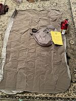 Full view of the beige Roots air mattress spread flat on floor with Roots branded gray carry bag and yellow instruction sheet on top.