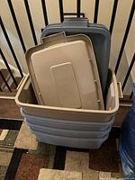 Four stacked Rubbermaid containers with lids, showing beige lids and blue container bodies.